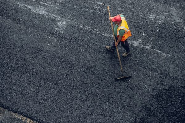 Workers lay a new asphalt coating using hot bitumen. Work of heavy machinery and paver. The view from the top