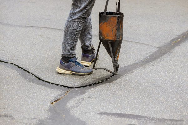 Workers restoration work sealing cracks applying liquid sealer to asphalt a road protective coat on roadway